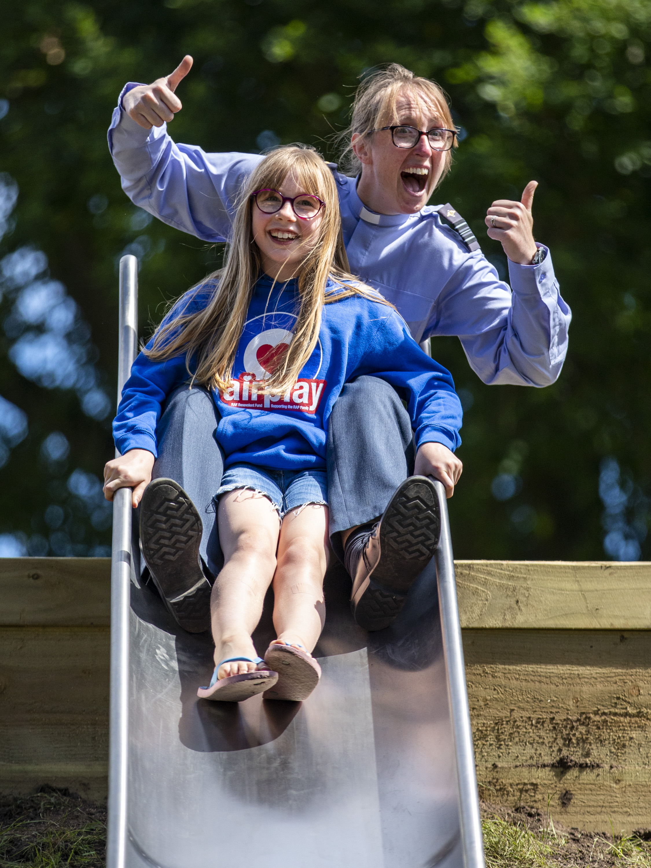 Image shows RAF Personnel with child going down an outdoors play park slide.